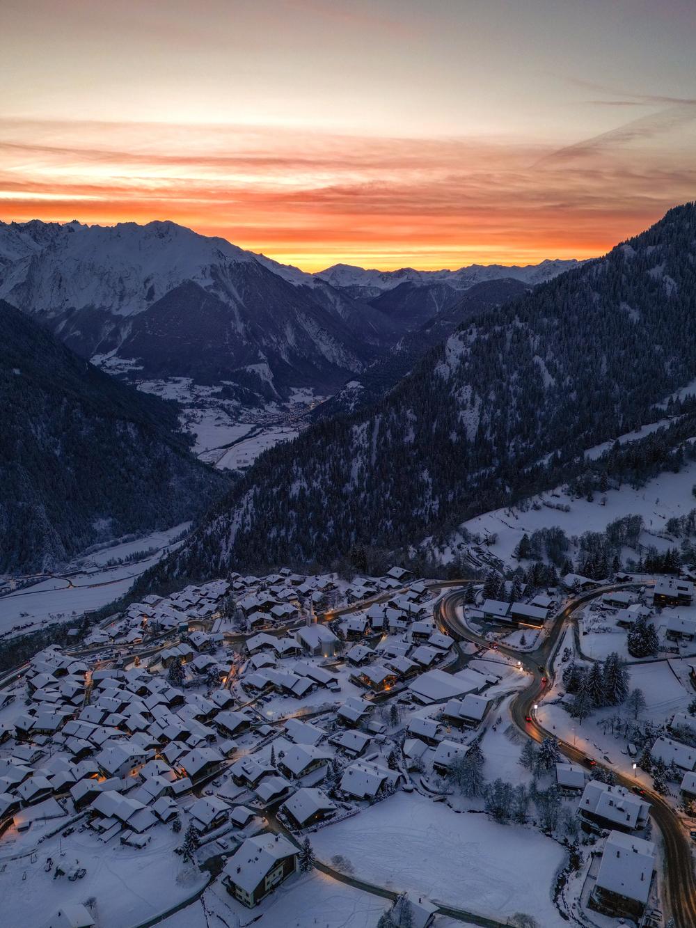 Aerial view at sunset from Verbier looking down the Val de Bagnes, a road winding through snowy chalets under an orange sky